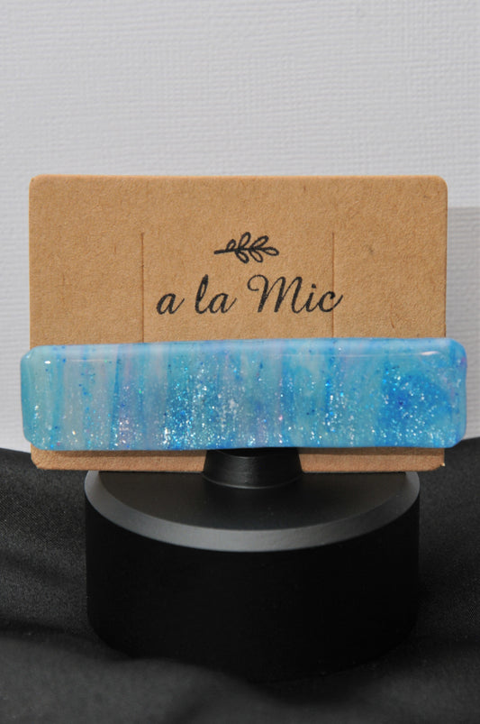 A blue and purple sparkle hair clip placed on a cardboard holder with the text 'A la mic'.